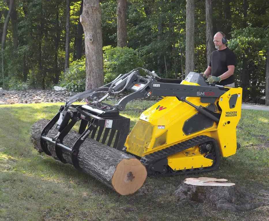 Mini-chargeuse SM100 déplaçant un tronc d'arbre
